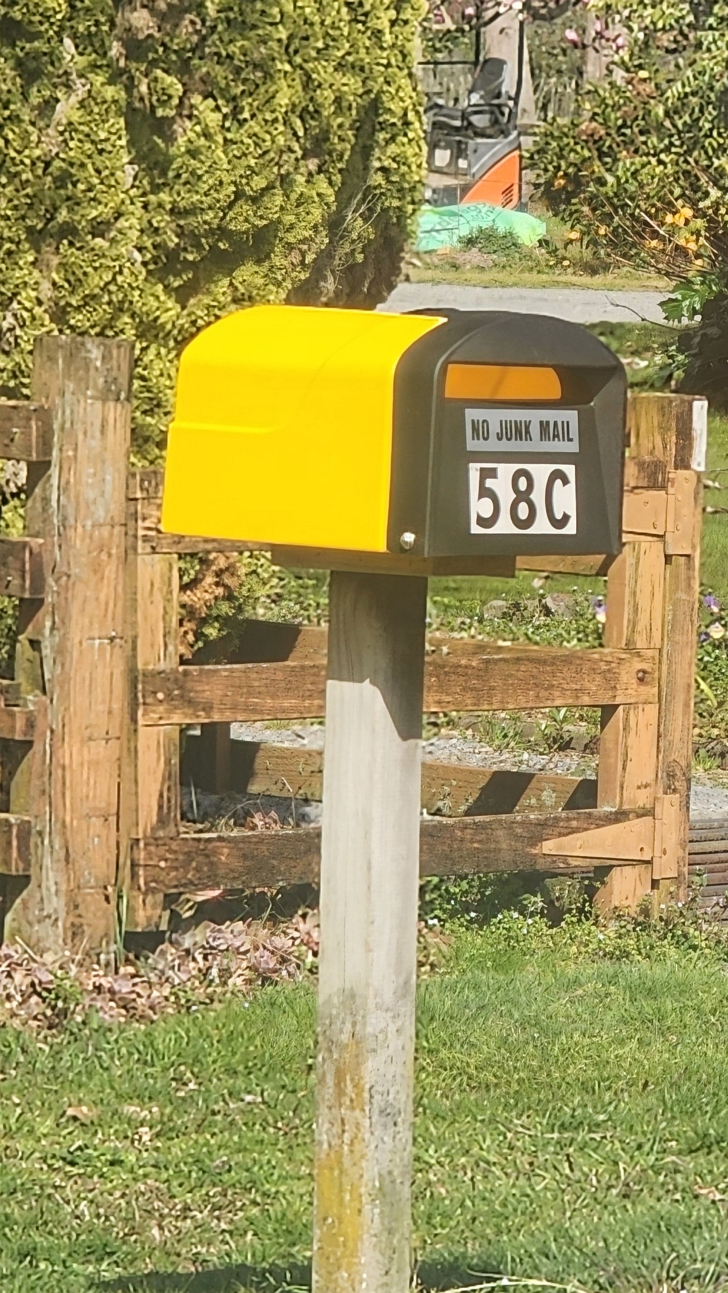 Two colorful mailboxes in a rural setting with a wooden fence and greenery.