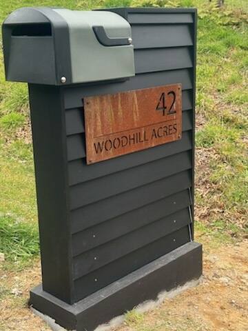 Black mailbox with a wooden plaque displaying '42 Woodhill Acres' on a grassy background.